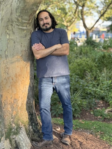 Carlos The Medium leans against a tree in Founders Park, Alexandria