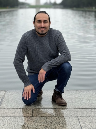 Carlos The Medium kneels by the edge of the Lincoln Memorial Reflecting Pool in Washington DC.